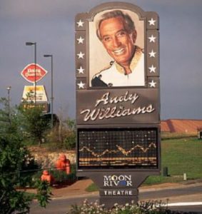ca. 1985-1995, Branson, Missouri, USA --- A giant picture of Andy Williams stands near the Moon River Theater, located on the "strip", a busy street in Branson lined with theaters, hotels, and restaurants. --- Image by © Buddy Mays/CORBIS